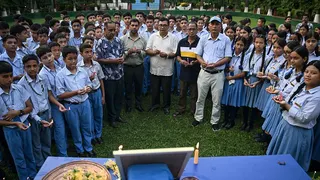 Students and a few men hold candles and stand around a blue table
