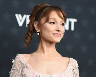 Ariana Grande with an updo hairstyle and drop earrings smiles at a red-carpet event