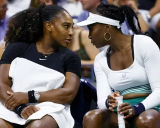 Serena and Venus Williams speak during a match on their bench.