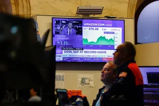 Traders at the New York Stock Exchange stand near a screen showing stock market data