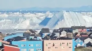 Iceberg collapsing creating wave near city with colourful houses