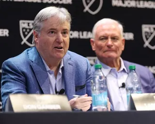Larry Berg, incoming MLS Commissioner, speaks at a press conference table beside another man