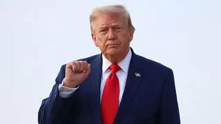 Donald Trump holds up his right fist while wearing a white shirt and red tie.