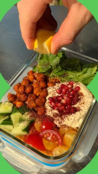Harissa couscous with crispy chickpeas in a food storage container with a lemon being squeezed on top of it