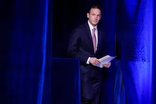 Man in suit stands on stage holding papers