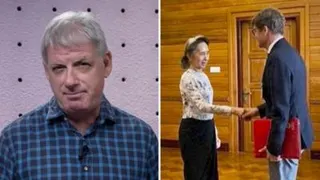 A man in a blue shirt speaks on the left, while a woman shakes a man's hand on the right.