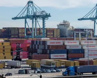 Stacked shipping containers and cranes fill the Port of Los Angeles with a truck passing by