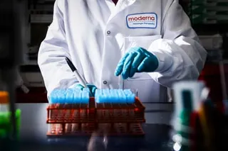a researcher in a white lab coat and gloves holds a vial