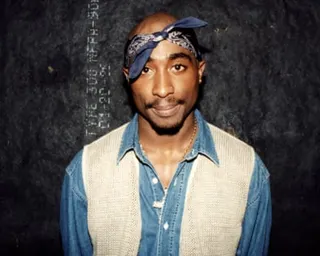 Rapper Tupac Shakur, wearing a bandana and denim layered outfit, poses backstage