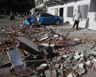 A crushed blue car sits amid earthquake rubble in Cali, Colombia, as a man walks nearby