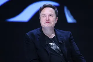 Elon Musk, in a dark blazer with a microphone on his lapel, smiles slightly during a discussion