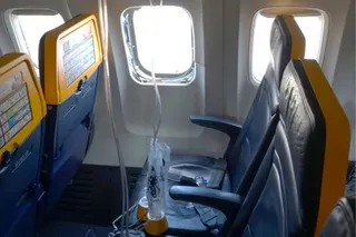 A view of a shattered window on a plane and oxygen masks hanging in front of seats.