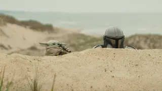 Grogu holds a spyglass while peeking over a sand dune alongside Din Djarin in The Mandalorian and Grogu.