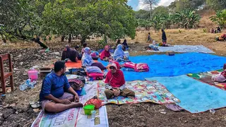 A group of people sit outdoors on blankets and tarps