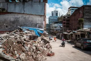 Motorists and pedestrians pass by the wreckage of a collapsed building on a street in Buenaventura. [Euan Wallace / Al Jazeera]