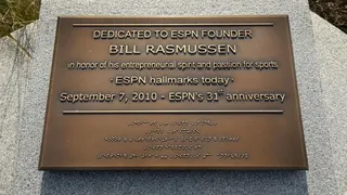 Bill Rasmussen stands beside a plaque dedicated to him as ESPN founder.