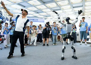 2026世界機器人大會19日在北京揭幕，圖為人形機器人的舞姿吸引外國觀眾圍觀拍照...