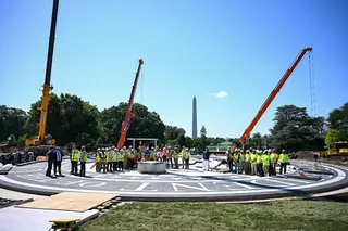 美国总统特朗普当地时间周三在白宫南草坪向媒体发表演说时，工人们在直升机停机坪的施工现场旁观看。（图取自法新社）