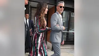 Sandra Bullock in multi-colored striped dress holds onto the arm of Bryan Randall in a grey suit