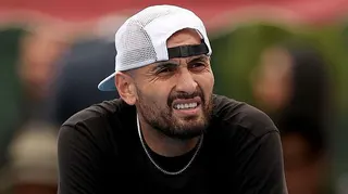 Nick Kyrgios, wearing a baseball cap backwards, looks out while slightly squinting