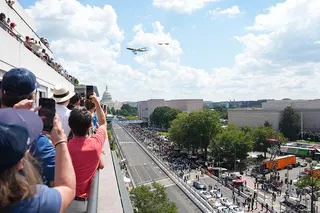 People take photos on a rooftop as Air Force one takes part in a flyover with the Capitol building in the background and the racetrack below