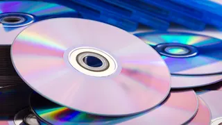 A pile of compact discs next to a pile of disc boxes.