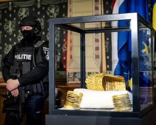 Recovered stolen golden helmet and bracelets displayed in a glass case, guarded by armed officer