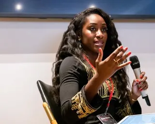 a woman speaks into a microphone with hand gestured while seated