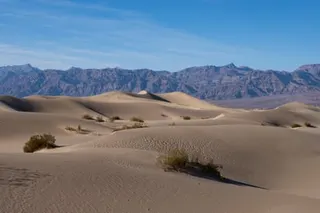sand dunes stretch toward rugged mountains under a blue sky