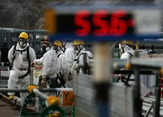Workers wearing protective suits and masks conduct a decommissioning operation near the No. 2 and No. 3 reactor buildings while a radiation monitoring post reads a radiation level of 55.6 microsieverts per hour at the tsunami-crippled Fukushima No. 1 nuclear power plant in Okuma, Fukushima Prefecture, in January.