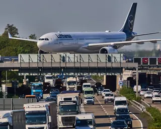 A Lufthansa plane rolls over a bridge spanning a busy motorway