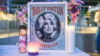 An illustration of Dolly Parton with her name stands on a table in front of a vase of pink lilies and behind three candles during the during a Seattle Community Vigil for Dolly Parton on Friday