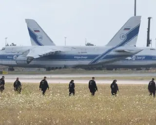 A line of police officers walk across a field at an airport with aircraft in the distance