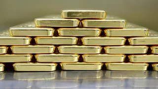 Gold bars are neatly stacked on top of each other to form a pyramid shape.