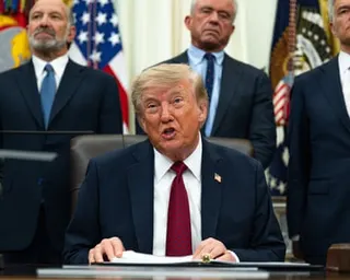 Donald Trump sitting behind a desk speaking while holding a form.