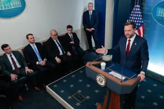 a man speaks into a microphone at a lectern as people sit nearby