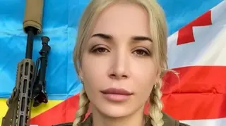 凱蒂·萊什卡謝利（Keti Leshkasheli）直視鏡頭。她留着金色長髮，編成兩條辮子。她身後可以看到一支槍，以及格魯吉亞和烏克蘭國旗。