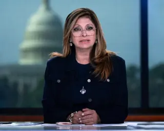 a woman speaks while seated at a desk in a television studio