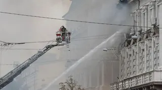 A firefighter on an extended platform helps with hosing down the building
